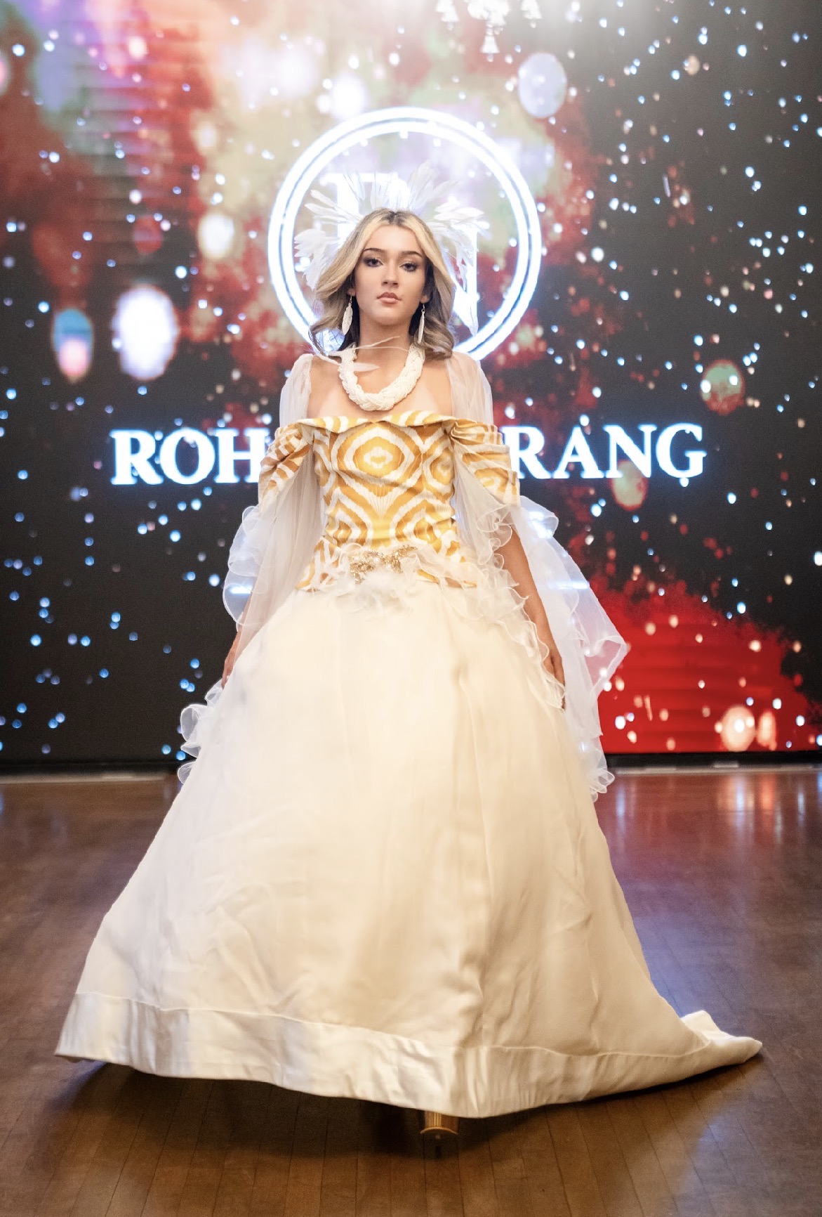 Model in a gold and ivory gown with a feathered headpiece on the Season 05 runway