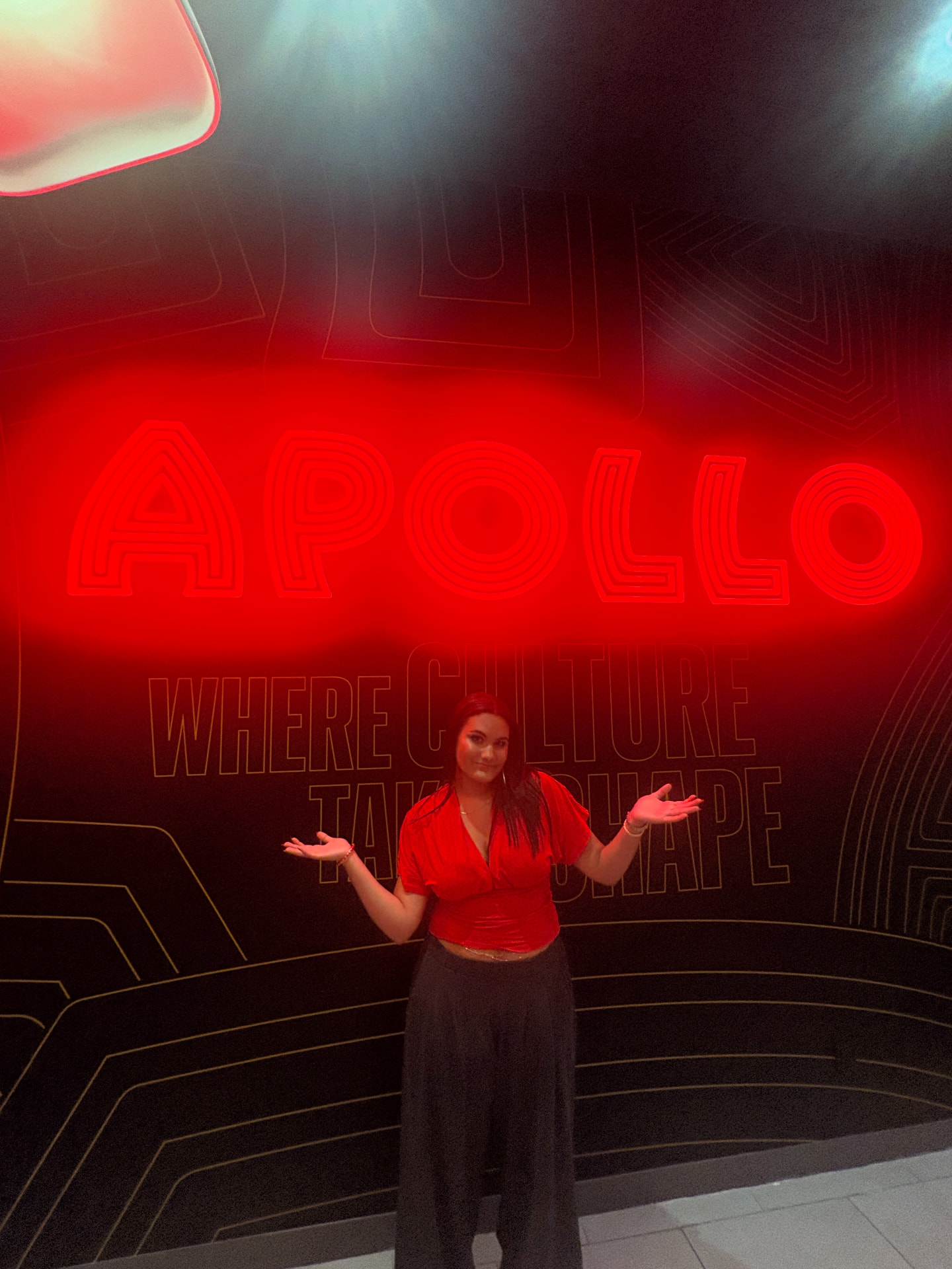Angelina Thompson in a red top beneath the illuminated red Apollo sign in Harlem during Teen Takeover