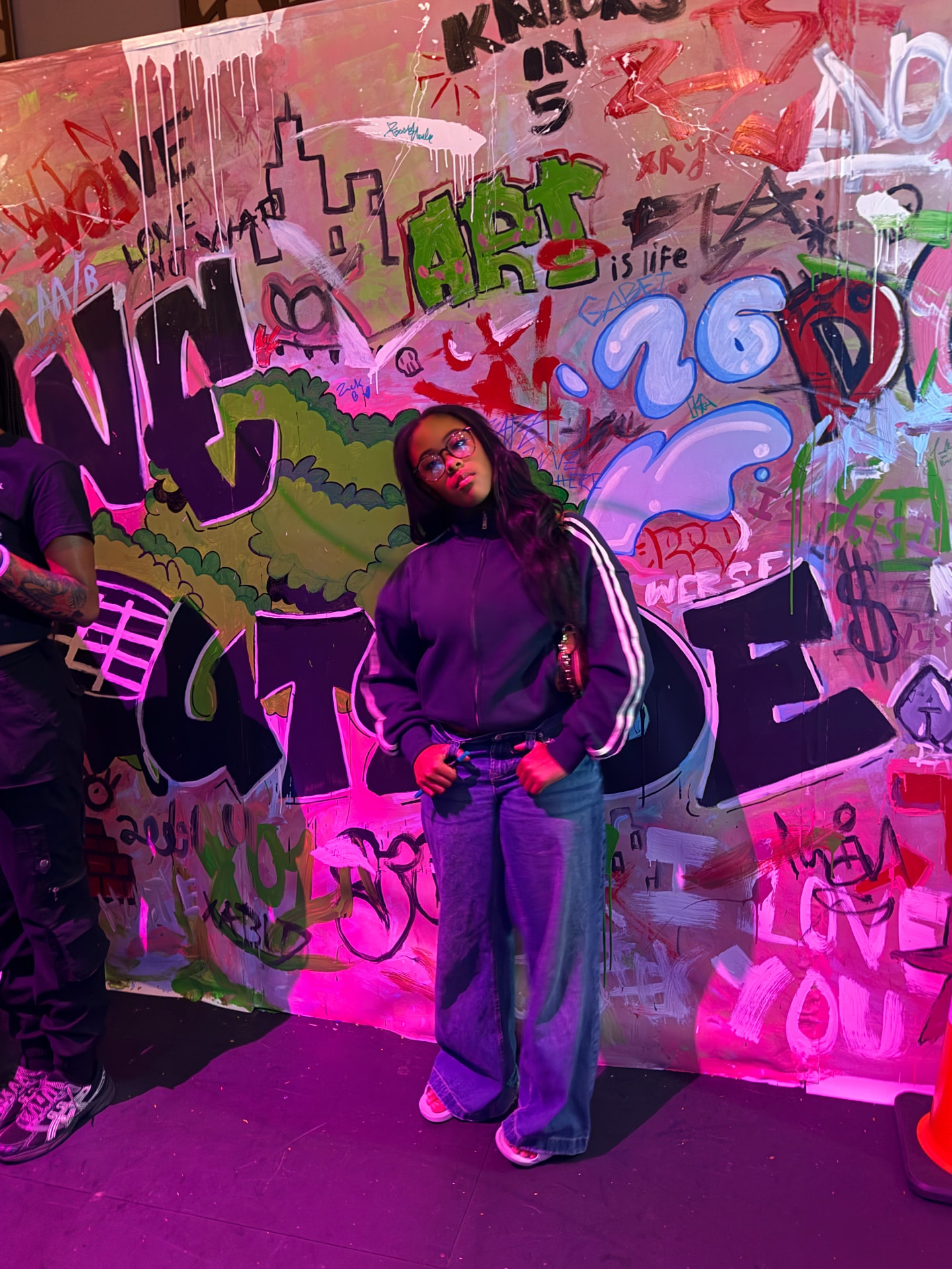 Aksana Antonius posing in front of the colorful Apollo Teen Takeover interactive graffiti wall