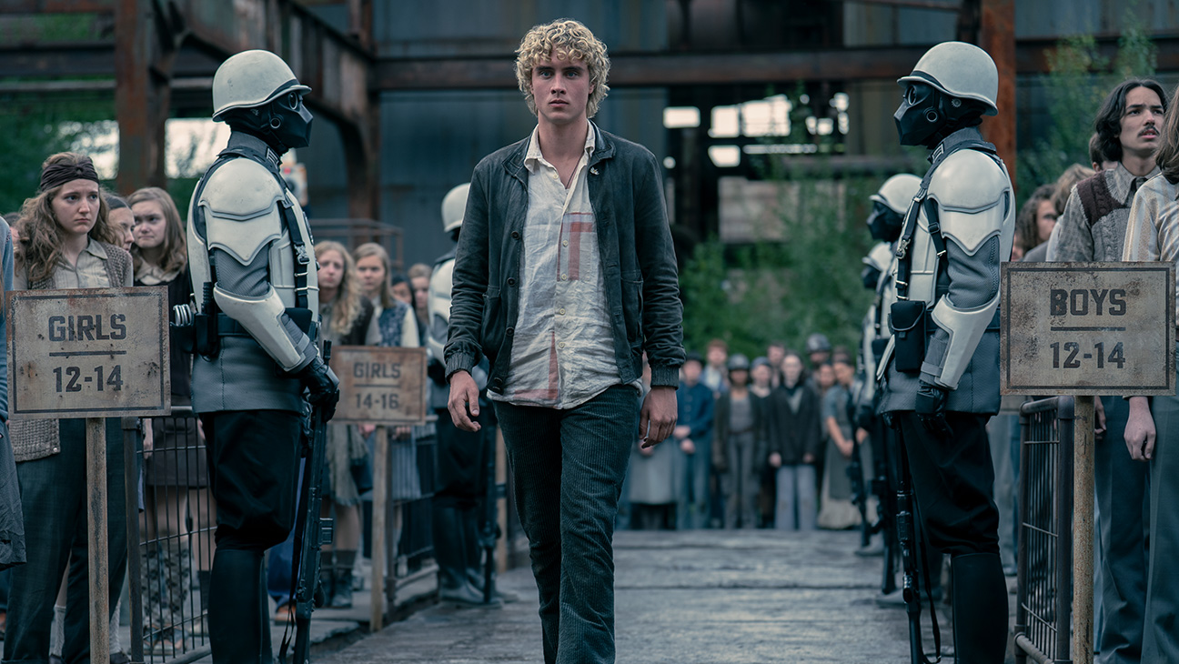 Joseph Zada as young Haymitch Abernathy walking between Peacekeepers in The Hunger Games: Sunrise on the Reaping.