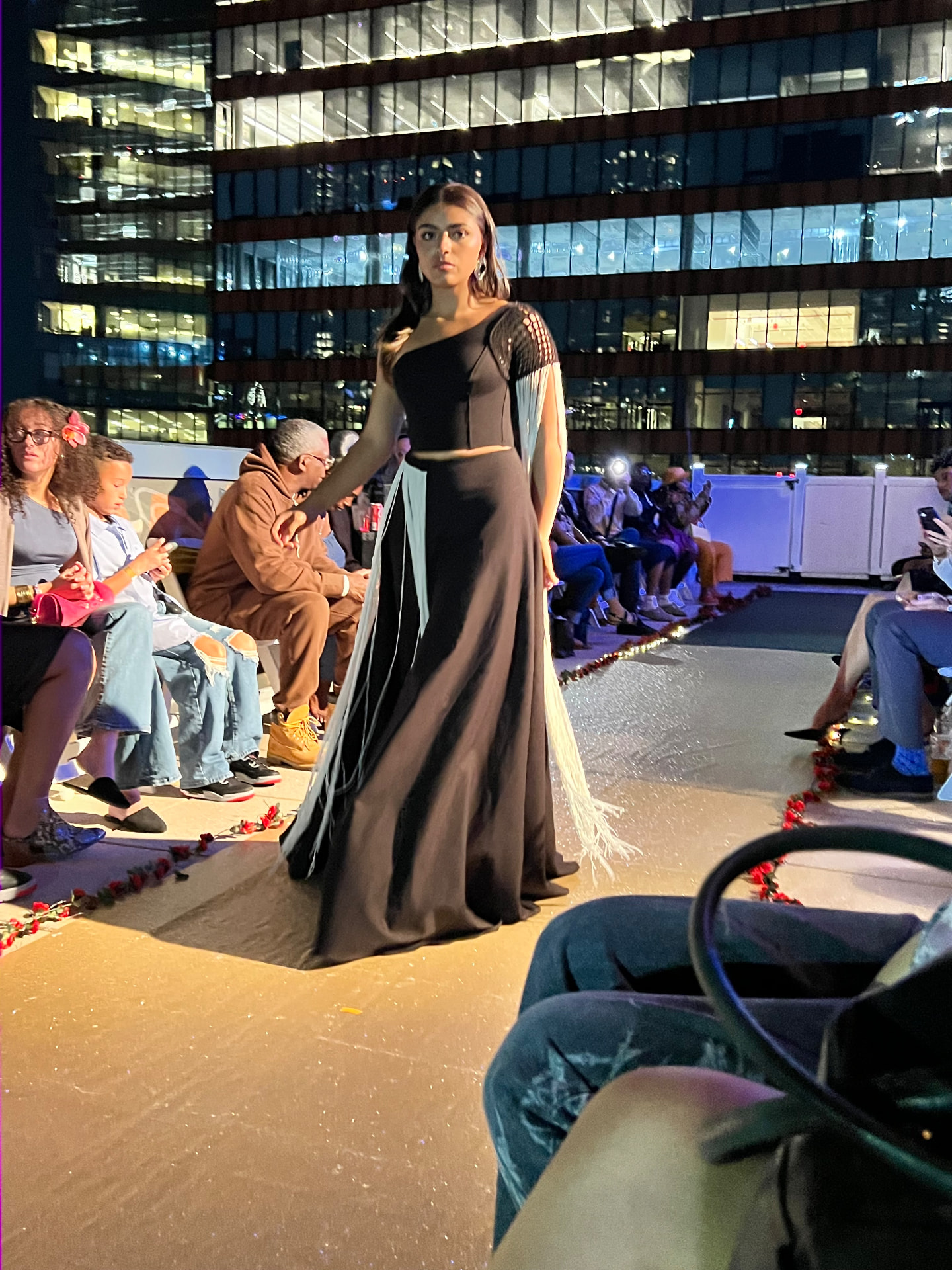 Model walking the A Designer's Dream runway in a black one-shoulder gown with fringe detailing.