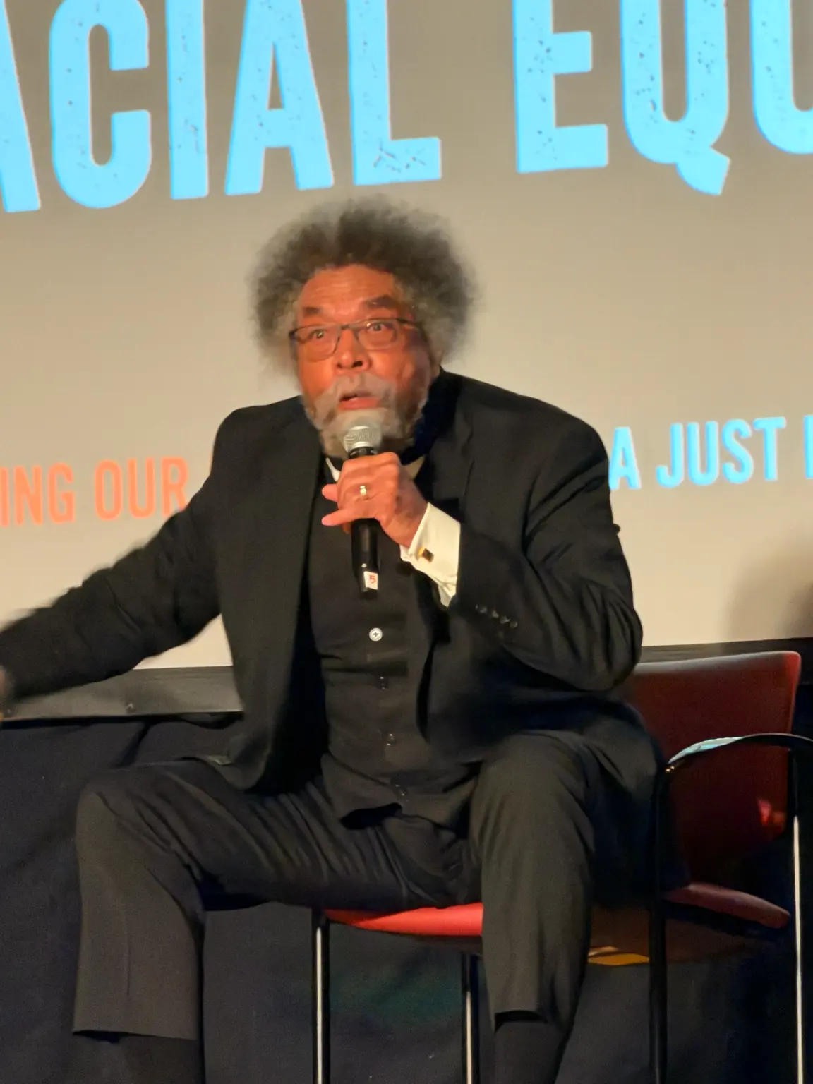 Dr. Cornel West speaking with a microphone on stage at Riverside Church