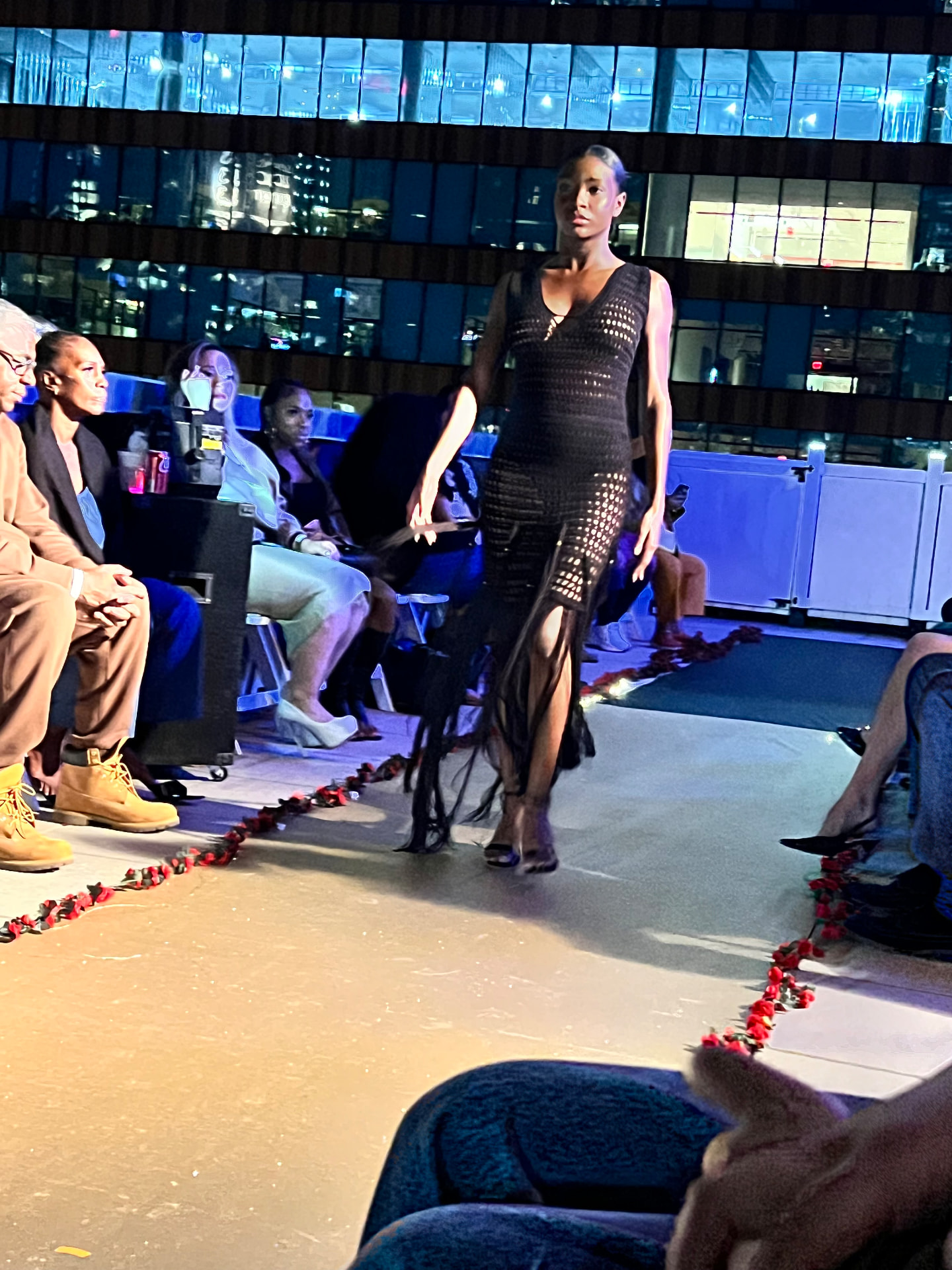 Model walking the A Designer's Dream runway in a black open-knit crochet dress with fringe hem.